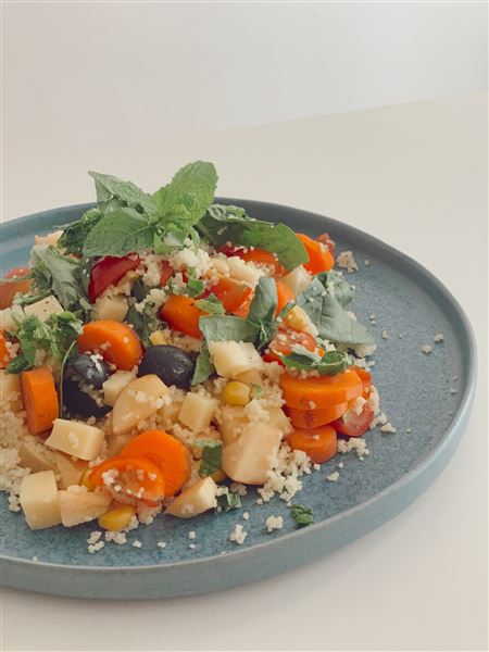 Cuscuz colorido com tomate-cereja, queijo, azeitonas e hortelã, num prato azul